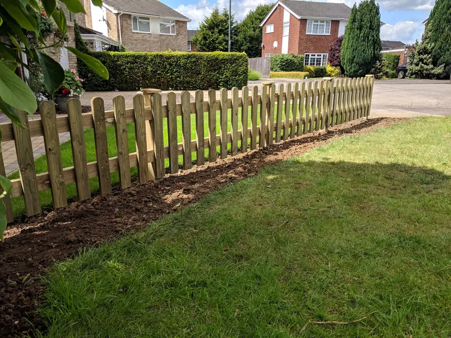 New timber picket fence installed along a front garden boundary with the soil made good behind it