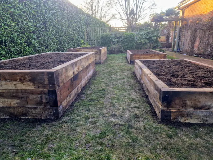 Four large raised beds built from railway sleepers on a lawn, filled with soil
